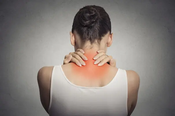 Frau sitzt nachdenklich auf dem Sofa und hält sich die Schulter vor Schmerzen